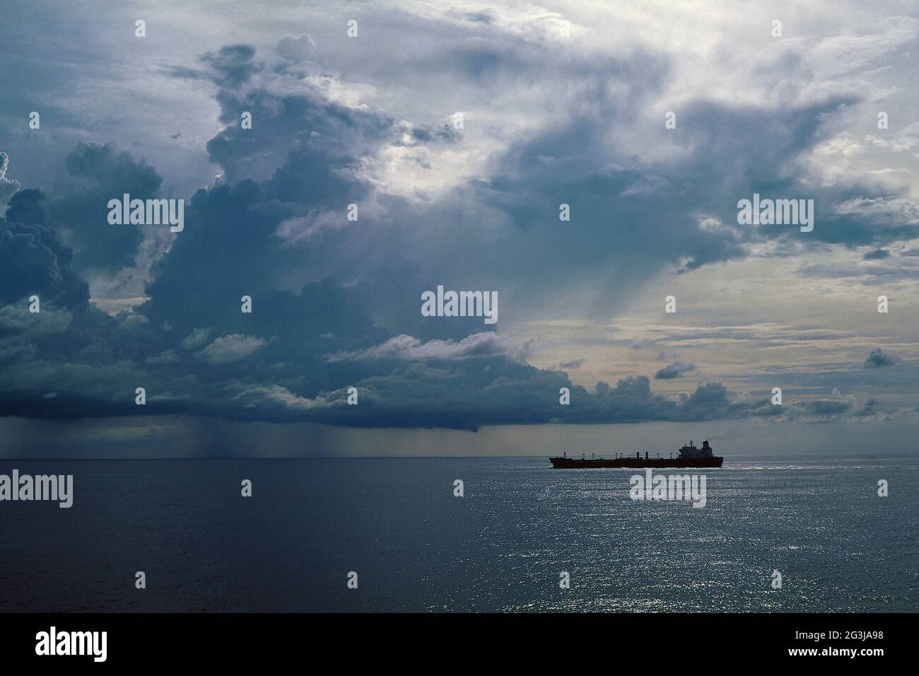 Landscape, seascape. A cargo ship, after departure,  proceeding in the ocean under the shadow of clouds Stock Photo