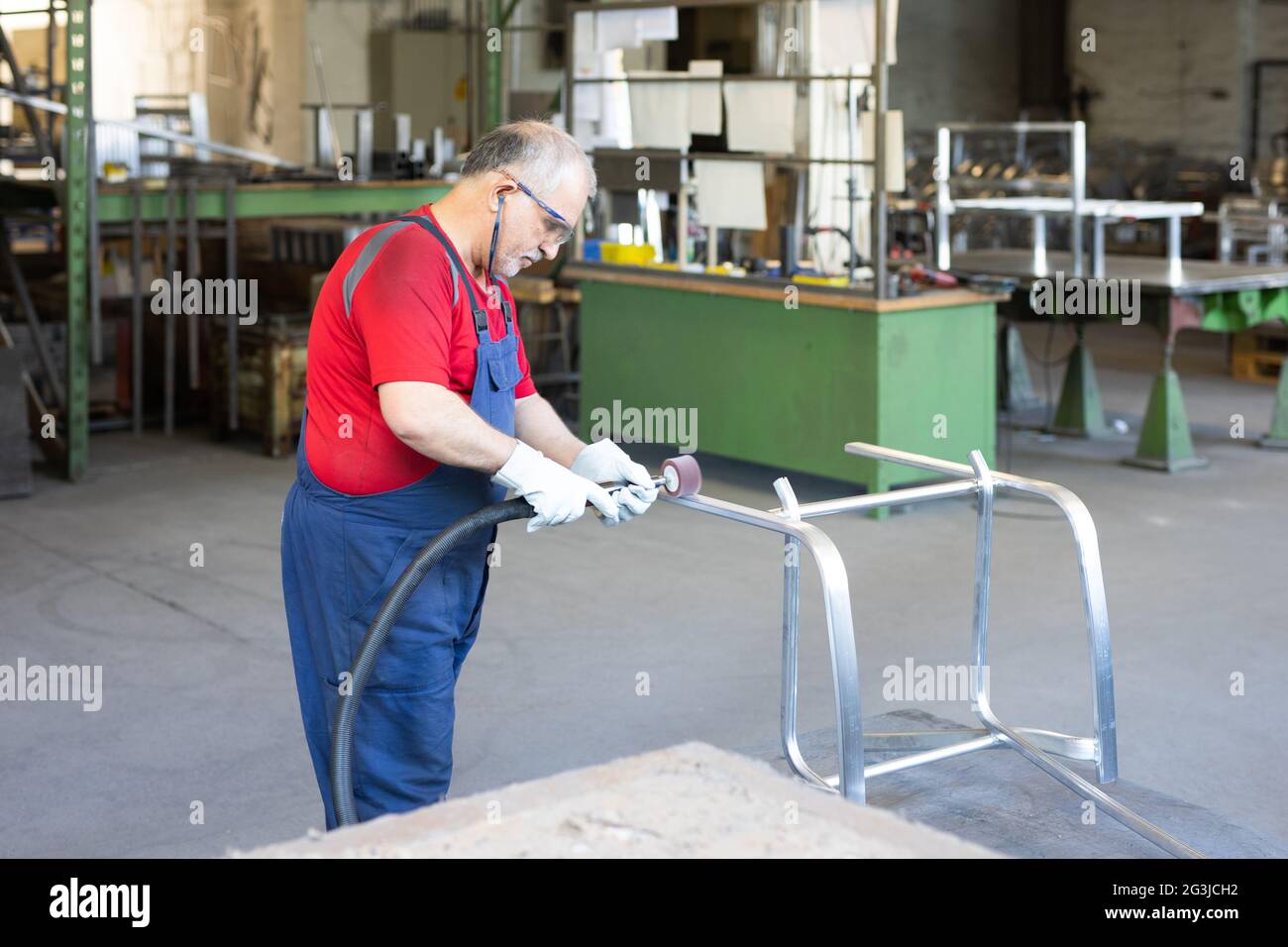 Blue collar worker polishing a piece of metal in a manufacturing facility. Polisher busy and concentrated whilst working in a factory. Stock Photo
