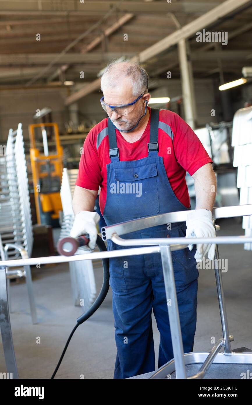 Blue collar worker polishing a piece of metal in a manufacturing facility. Polisher craftsman busy and concentrated whilst working in a factory. Stock Photo