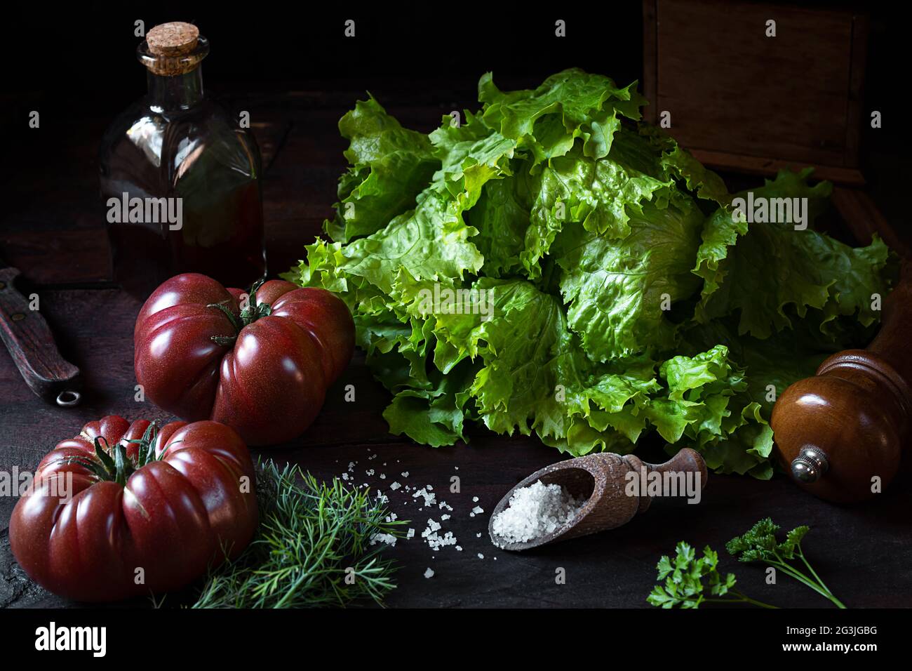 Fresh organic salad, tomatoes, a bottle with pumpkin seed oil on an old wooden table, the concept of healthy eating and vegetarianism, low key style Stock Photo