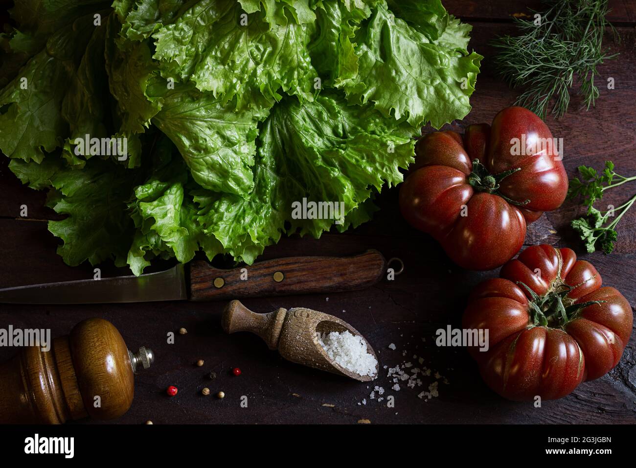 Fresh organic salad from a vegetable garden and tomatoes on an old wooden table, the concept of growing your own food and vegetarianism, top view, rus Stock Photo