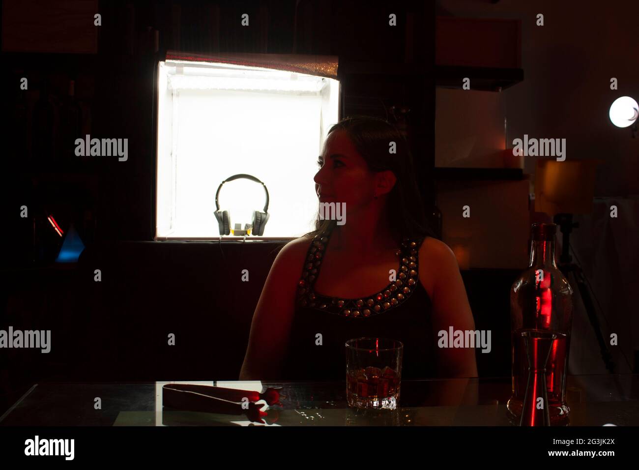 Waitress behind the counter of a bar listening attentively to requests next to a glass of whiskey on the rocks that she served Stock Photo