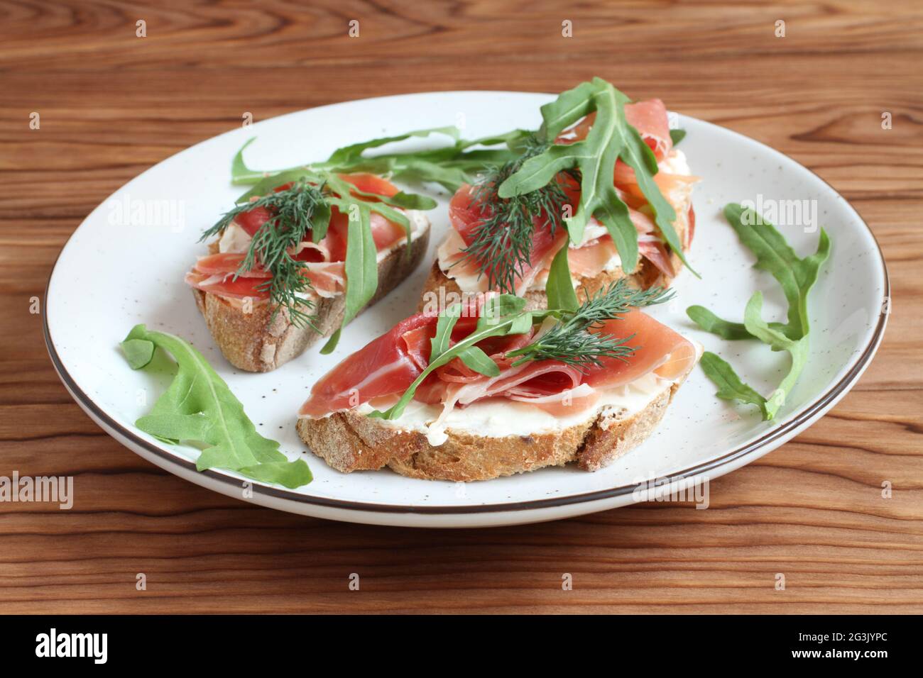 Buckwheat toasts with goat cheese, ham and arugula lying on a white plate on a wooden table.  Closeup Stock Photo