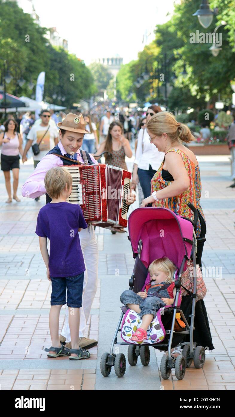 A Bulgarian accordion player interactiion with a curious boy on Vitosha Boulevard in Sofia, Bulgaria. Stock Photo