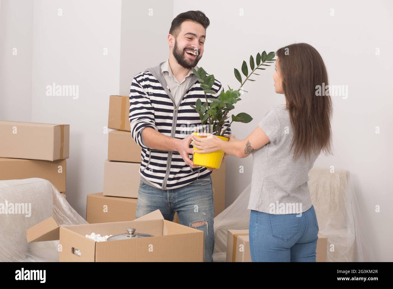 Excited young couple moving home standing close together with plants in their hands. Stock Photo