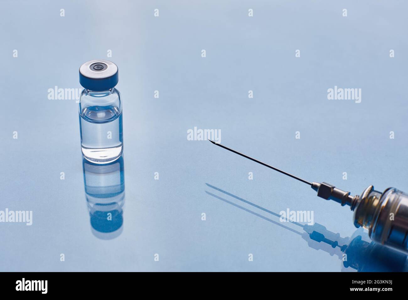 Glass vaccine vial and glass medical syringe on blue glass background ...