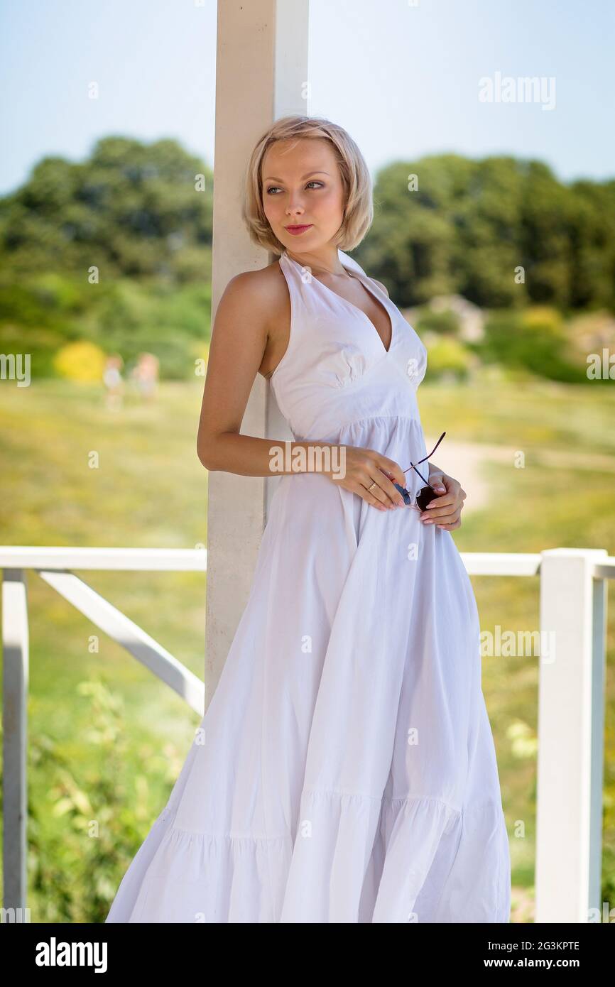 Blond young female in long white dress standing in alcove. Stock Photo