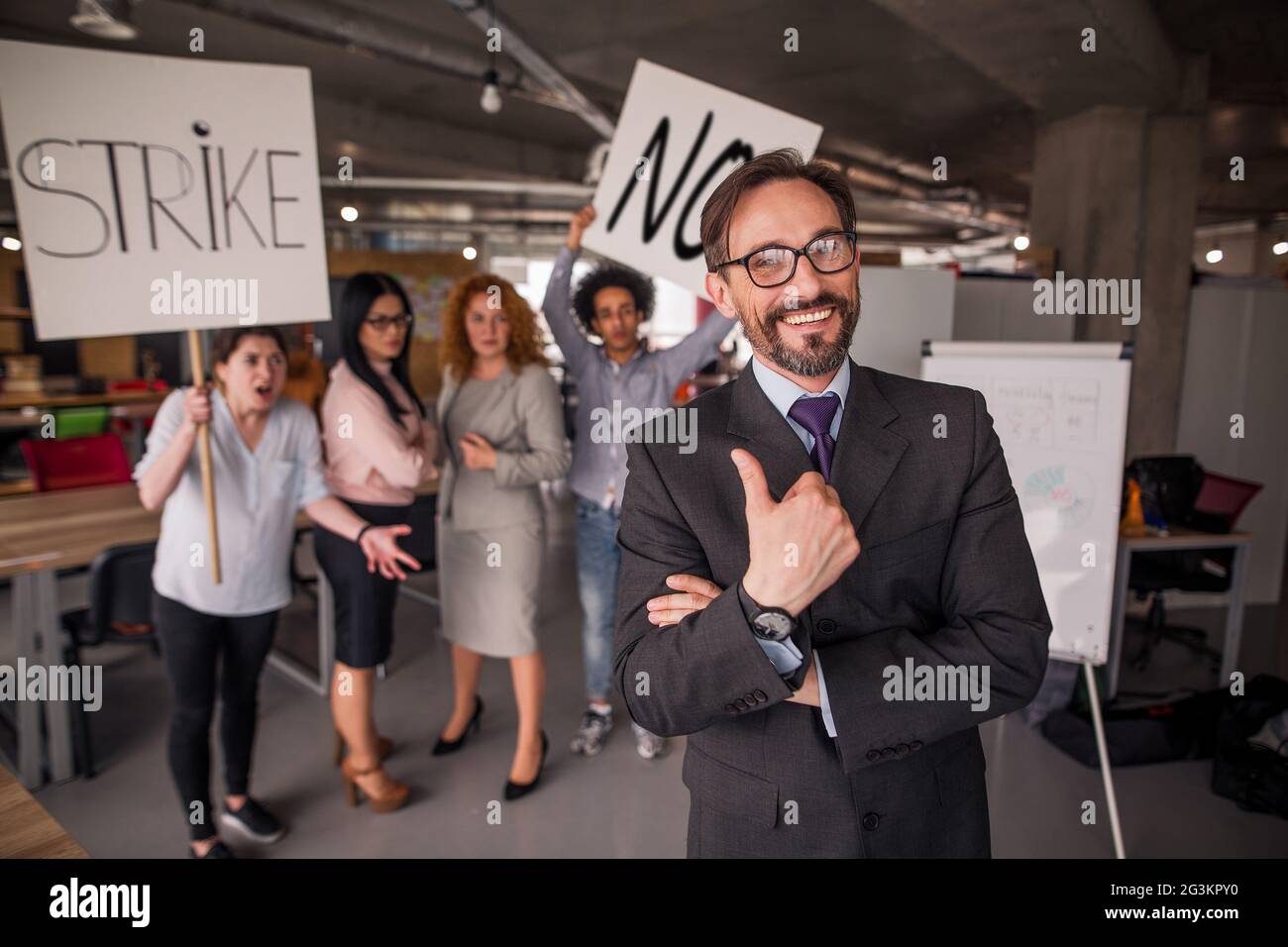 Laughing director showing thumb up, striking employees on backdrop. Stock Photo