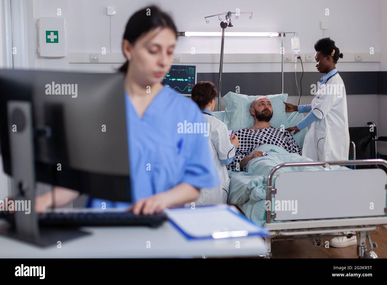 Front view of asisstant typing medical expertise on computer while in background black practitioner doctor discussing with sick man healthcare treatment. Hospitalized patient having respiratory disorder Stock Photo