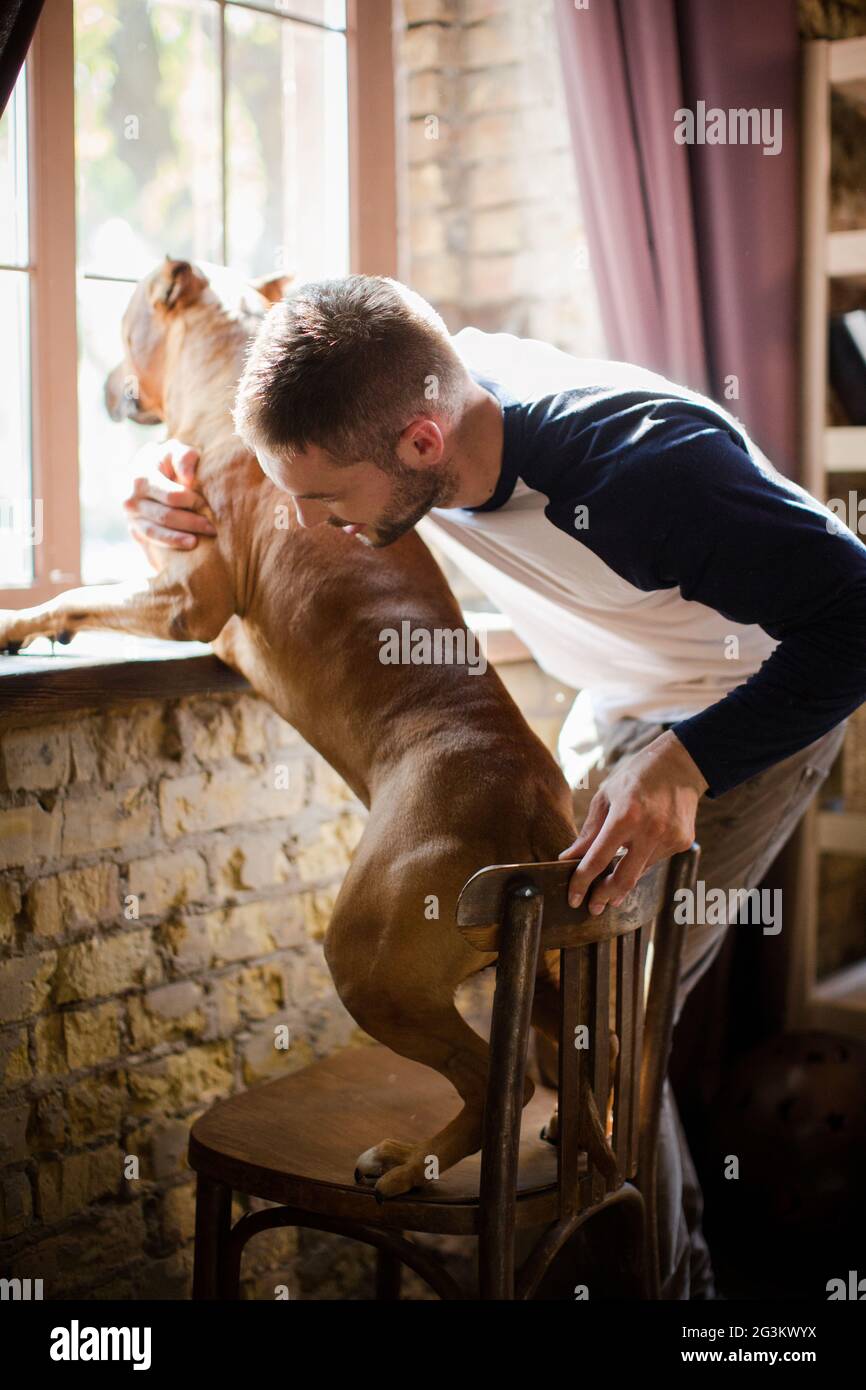 Sportive male and his dog standing by windowsill. Stock Photo