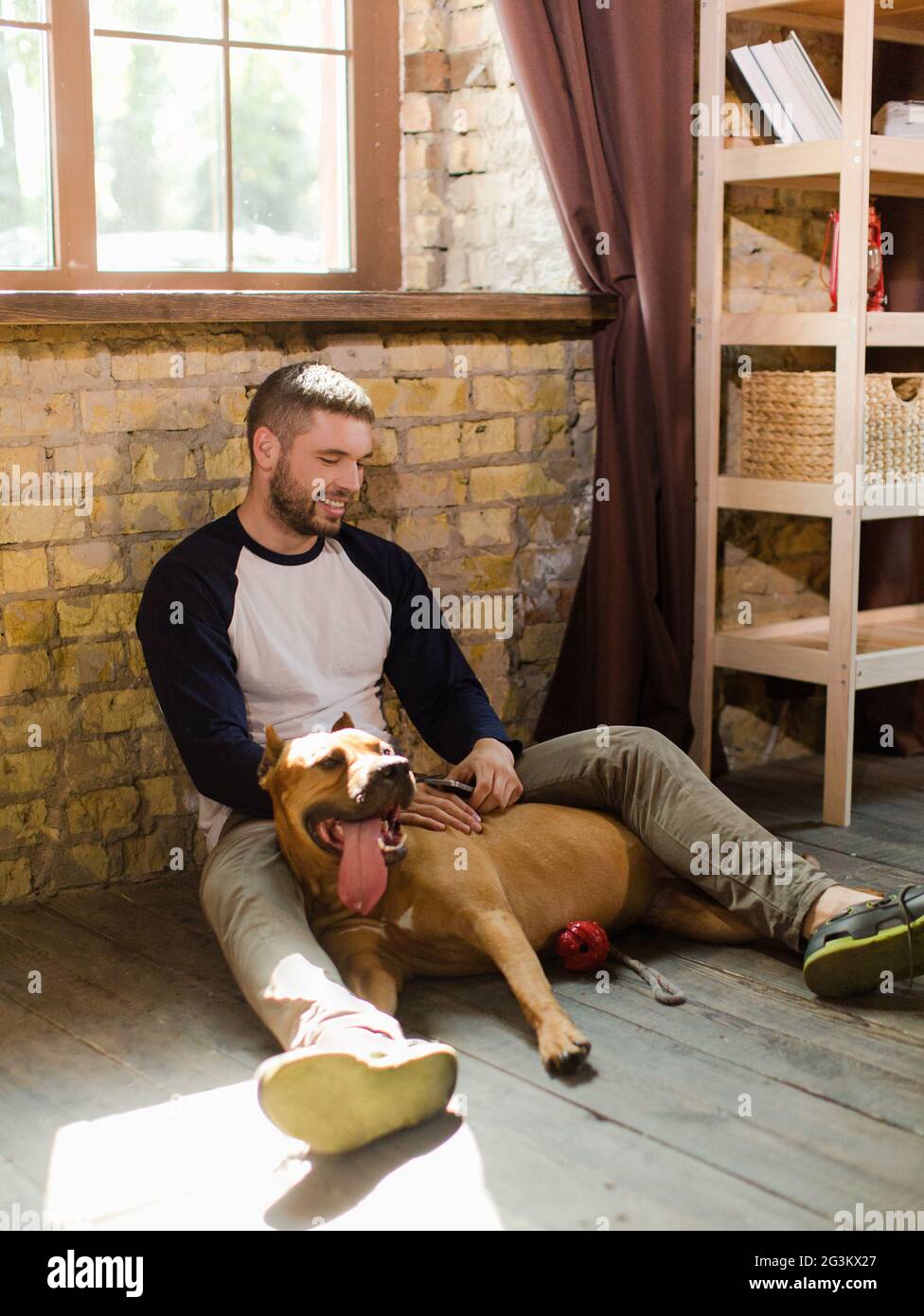 View of young sportive man having fun with dog at home. Stock Photo