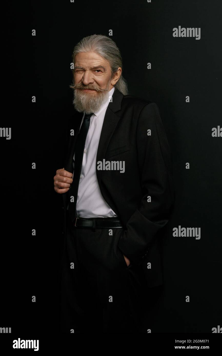 Old man in black suit and white shirt standing against black background. Stock Photo