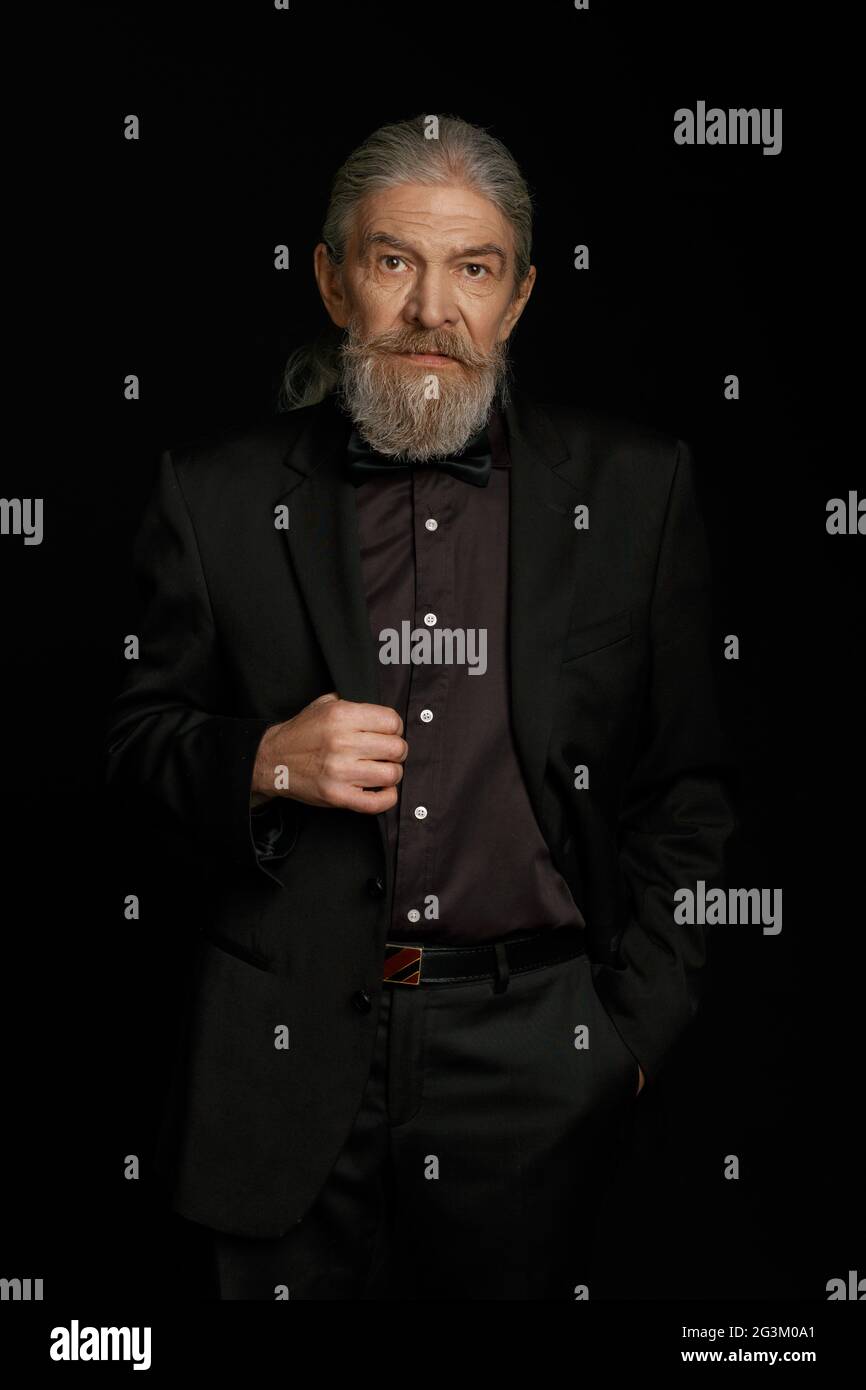 Old man in dark clothes on black background. Stock Photo