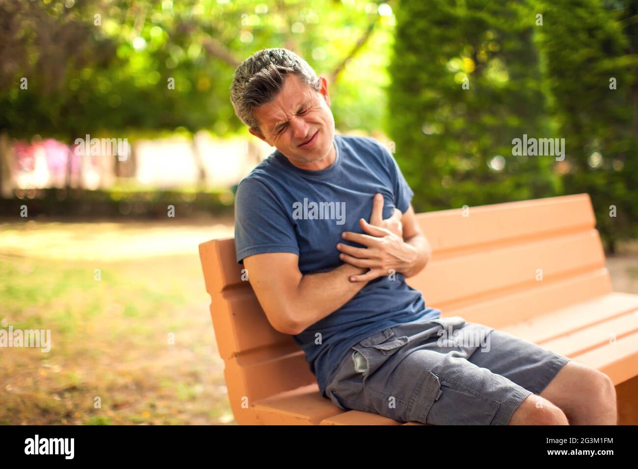 Man with heart pain outdoor. Male feeling chest pain sitting on the bench in the park. Healthcare and medicine concept Stock Photo