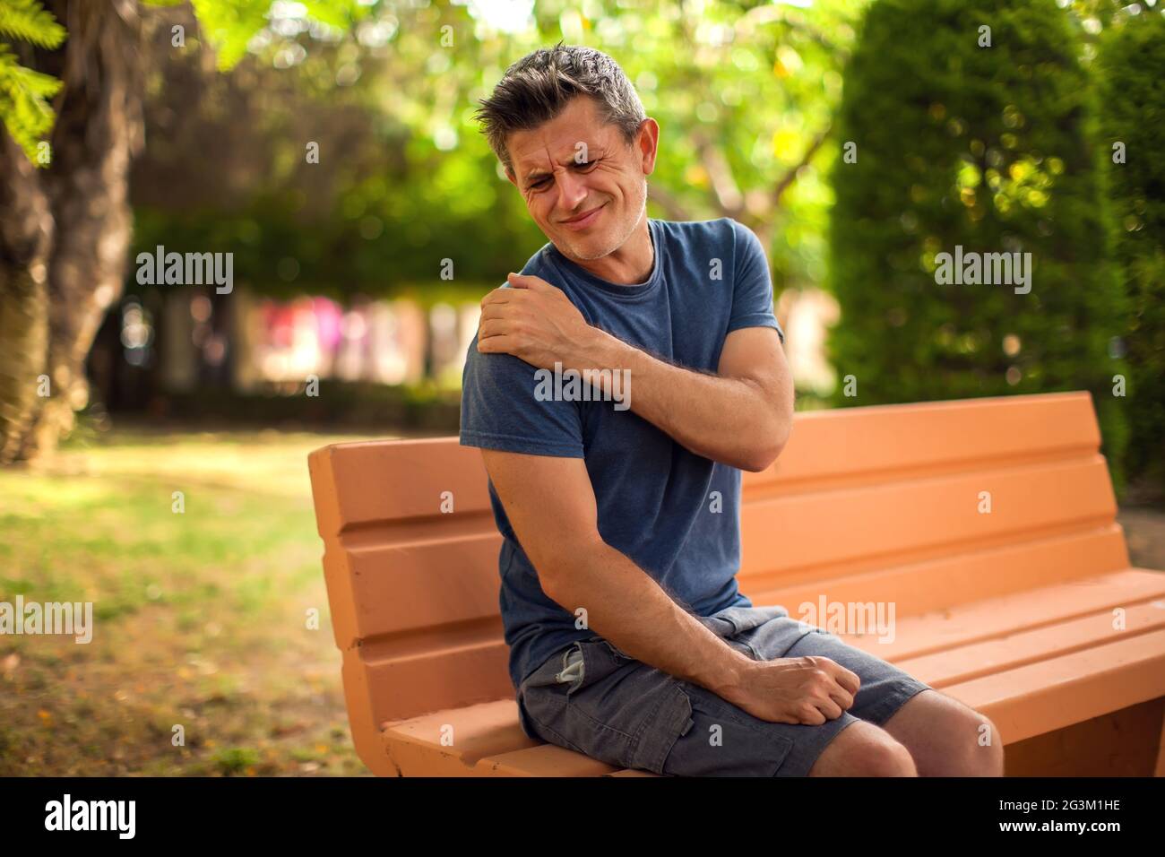 Man with shoulder pain sitting on the bench in the park. Healthcare and medicine concept Stock Photo