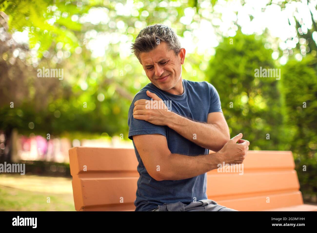 Man with shoulder pain sitting on the bench in the park. Healthcare and medicine concept Stock Photo