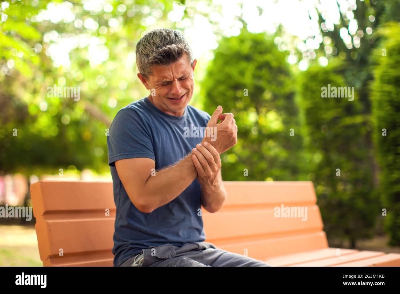 Man feeling arm pain sitting on the bench in the park. Healthcare and medicine concept Stock