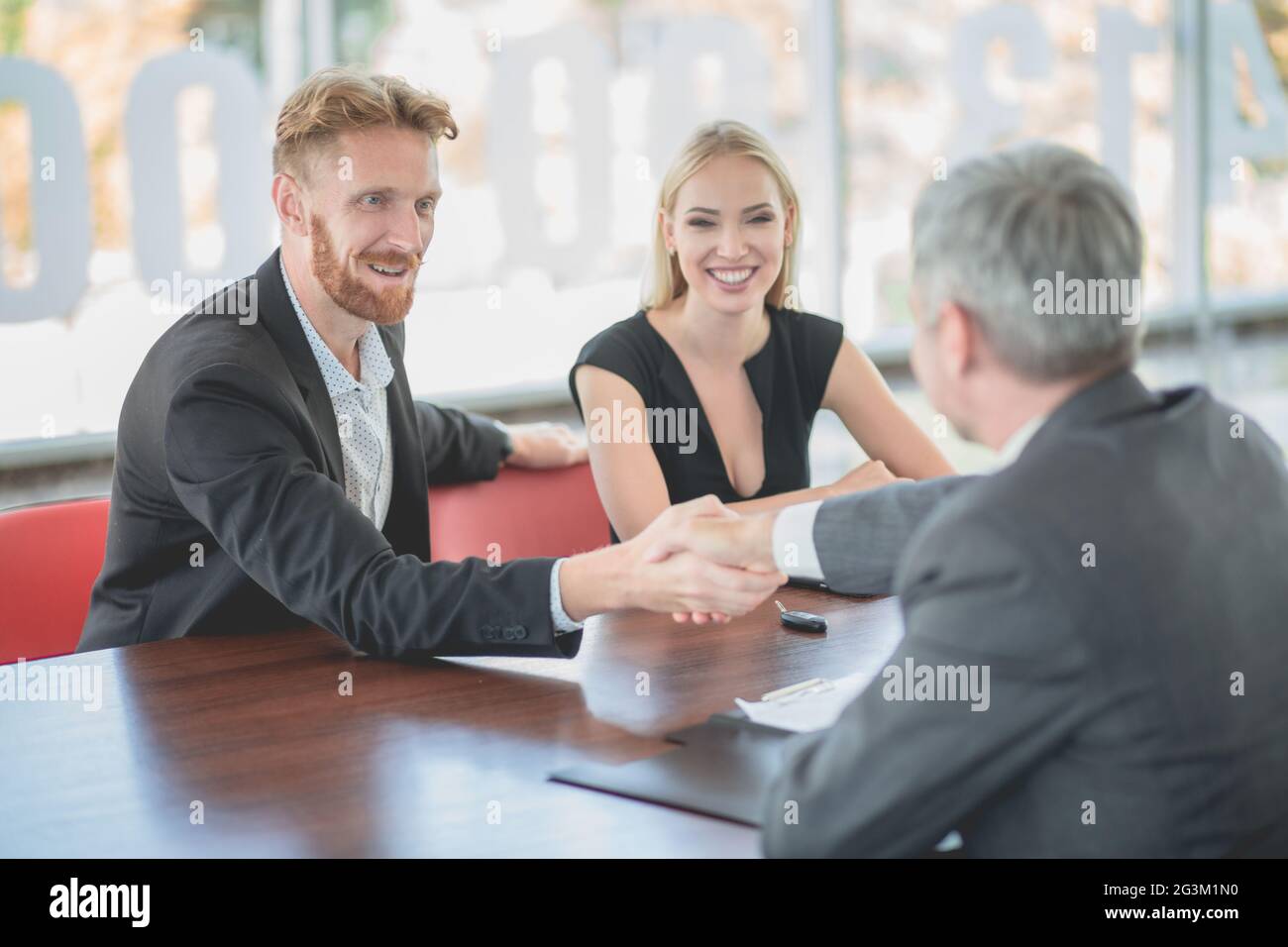 Happy young couple bying new car, signing documents with dealer. Stock Photo