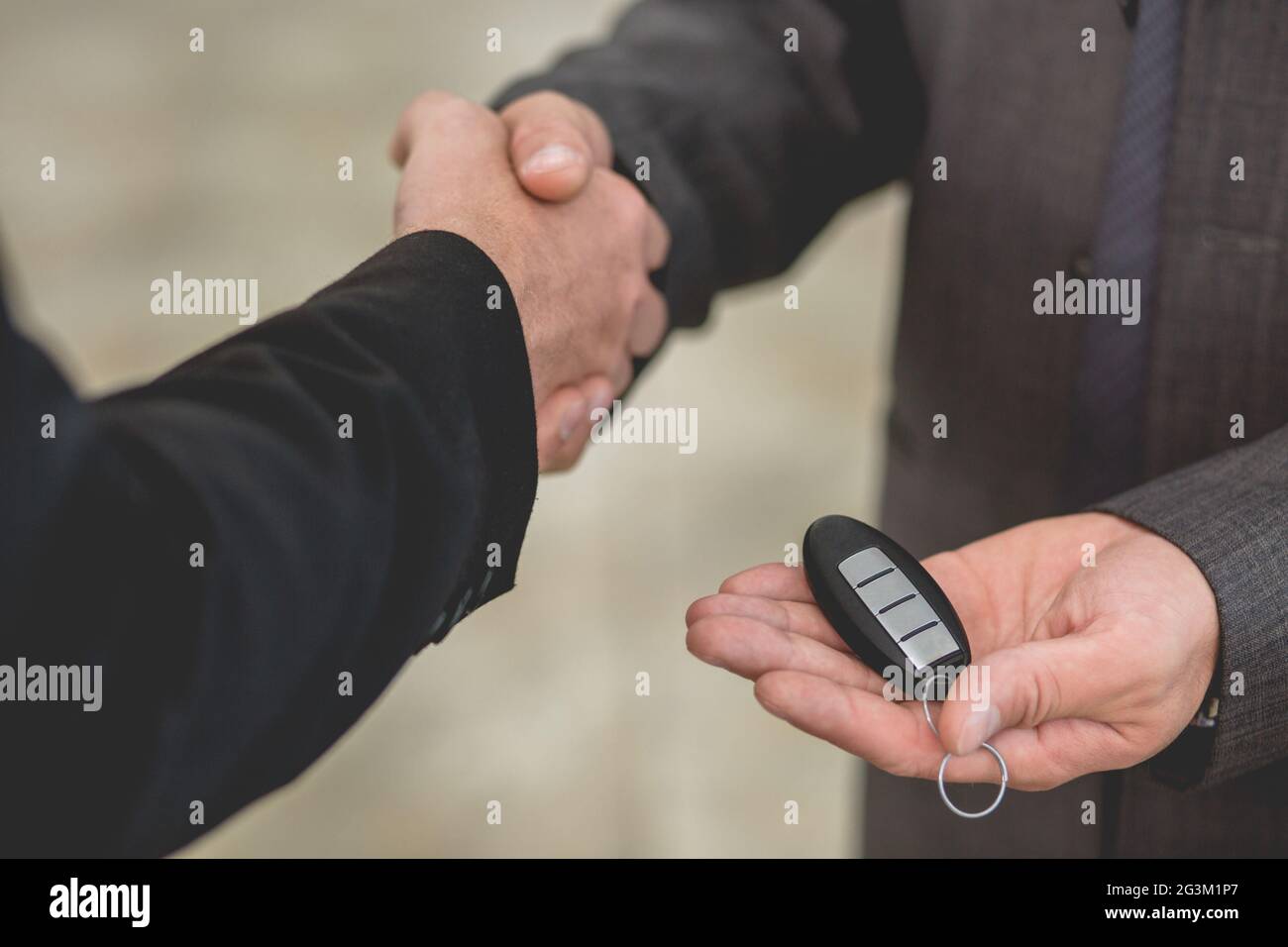 Vehicle dealer passing keys from new car to happy young man. Stock Photo