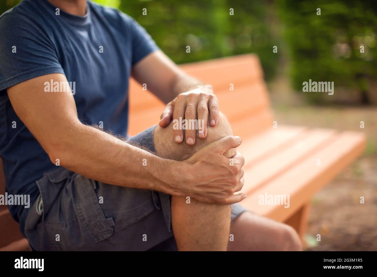 Man with knee pain sitting on the bench in the park. Healthcare and