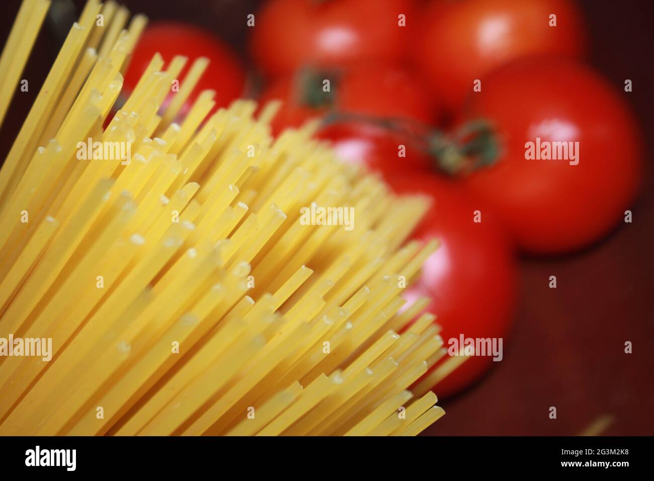 Uncooked spaghetti and tomato closeup photography on a wood background. Stock Photo