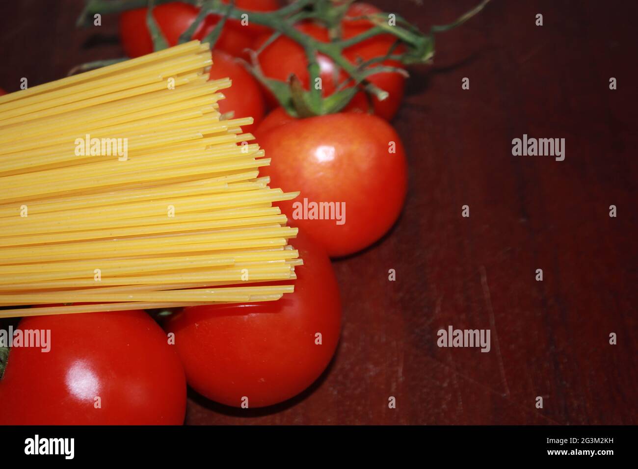 Uncooked spaghetti and tomato closeup photography on a wood background. Stock Photo