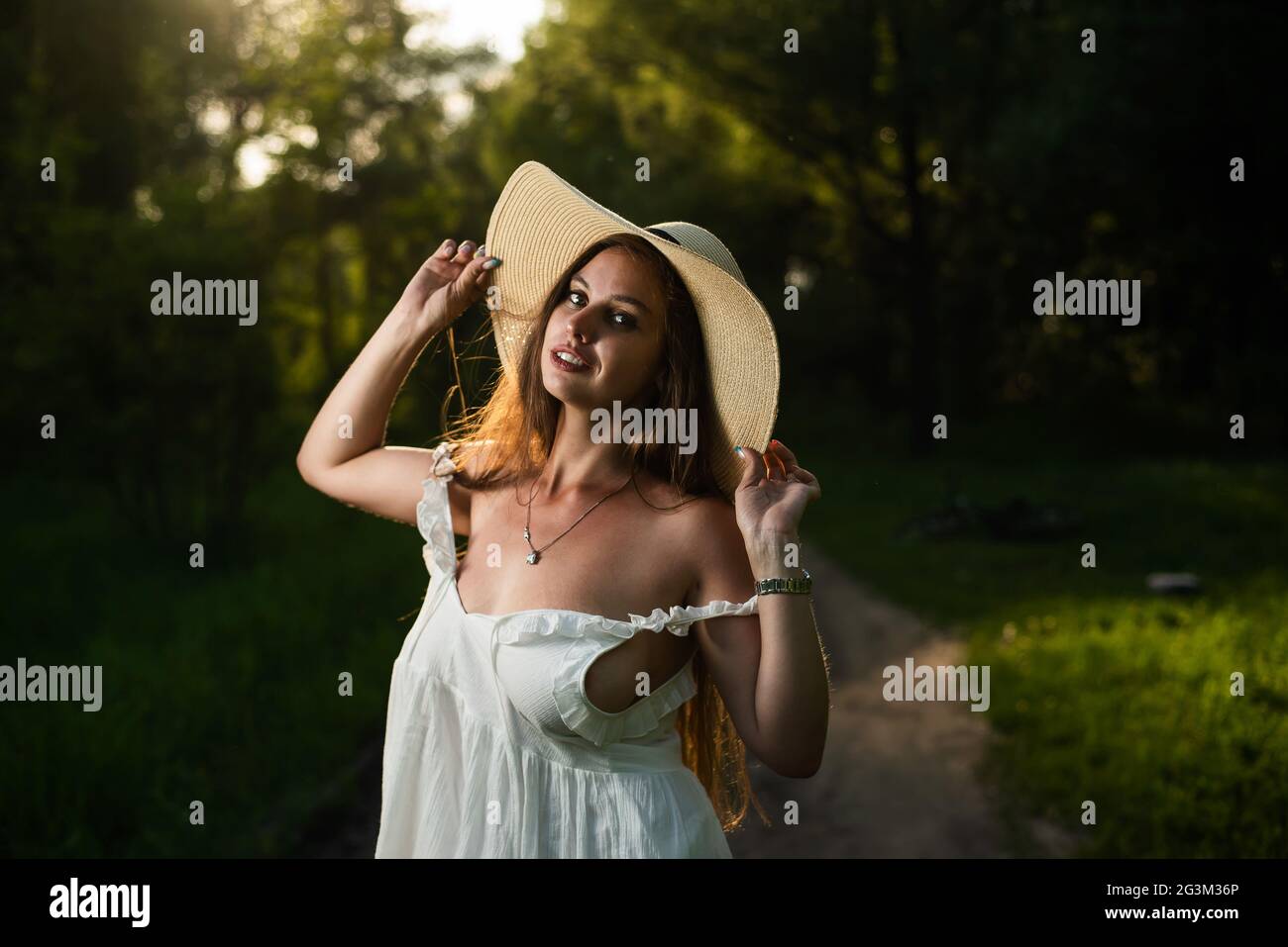 Beautiful caucasian woman in a white dress and straw hat in the forest ...
