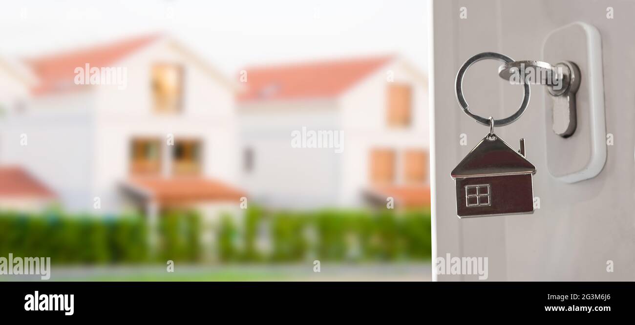 house keys in the door in the foreground with houses in the background Stock Photo
