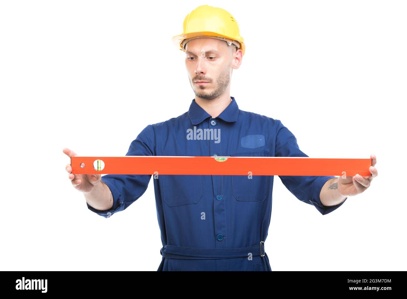 Portrait of successful handsome young adult Caucasian construction engineer wearing uniform with hardhat measuring level of something Stock Photo