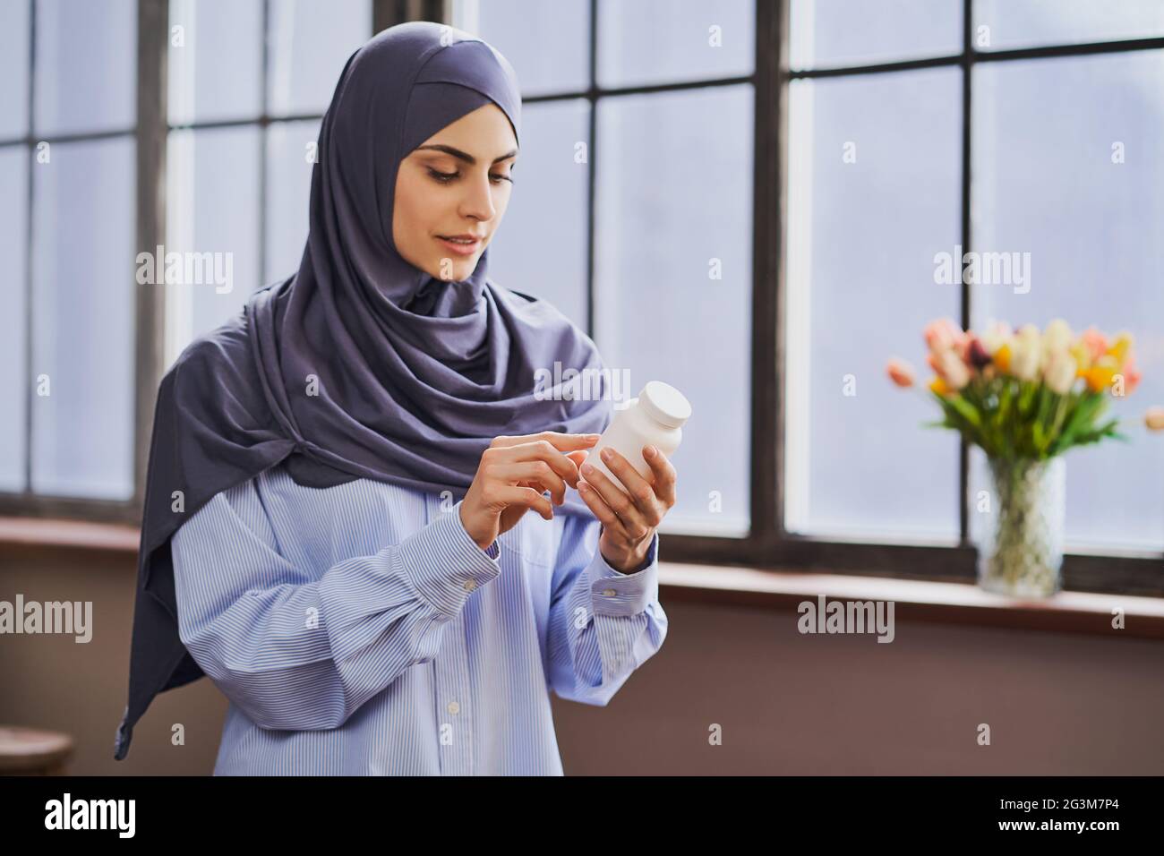 Muslim woman holding a bottle of pills and reading the list of ingredients Stock Photo