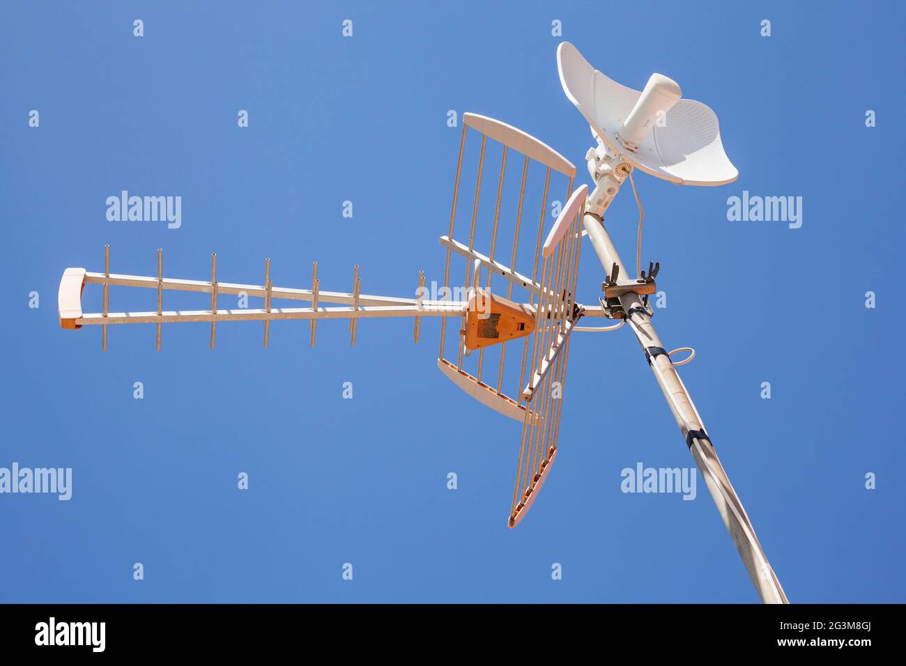 Television and internet antennas installed on a metal mast with the clear blue sky in the background. Stock Photo