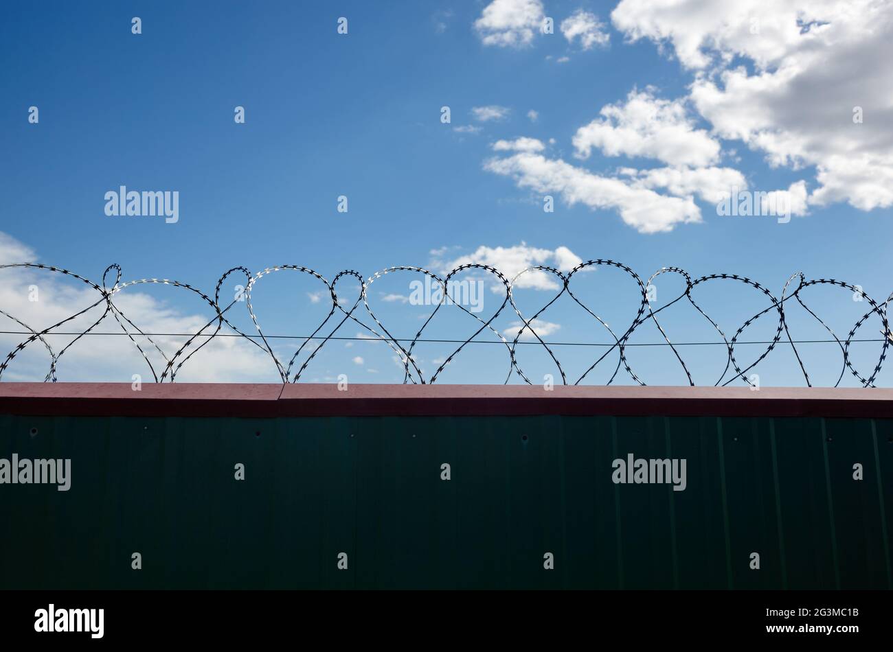 Metal wall with barbed wire against the blue sky background. Fence with barbwire for protection, space for text Stock Photo