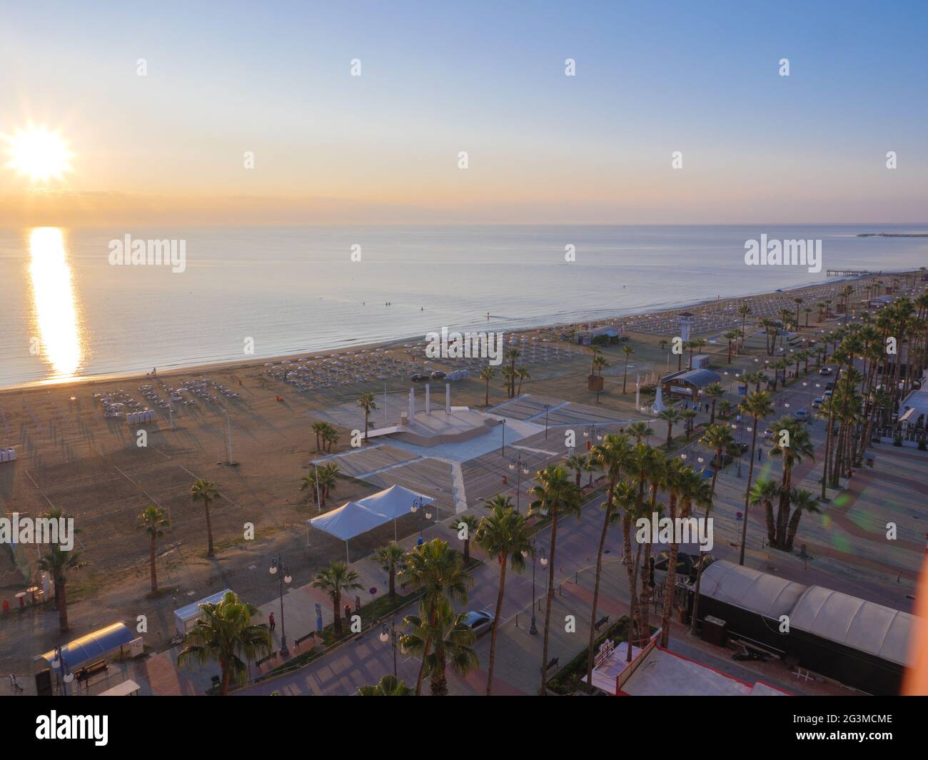 Top aerial view overlooking the break of the day at the Finnikoudes palm tree promenade in Larnaca old town, Cyprus. Rising sun glade at sea surface. Stock Photo