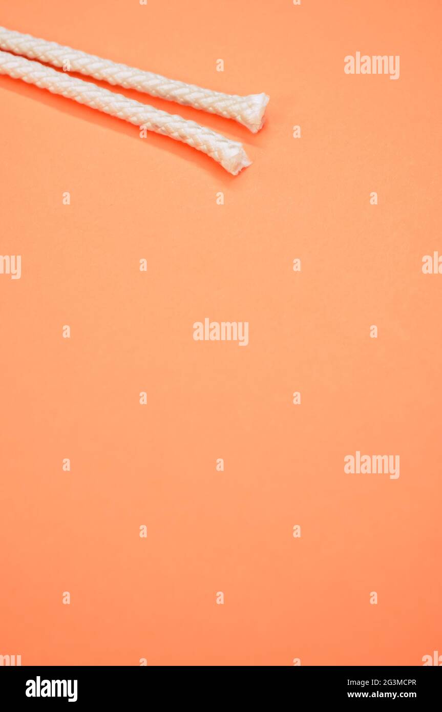 Vertical shot of two white short ropes isolated on the pastel orange ...