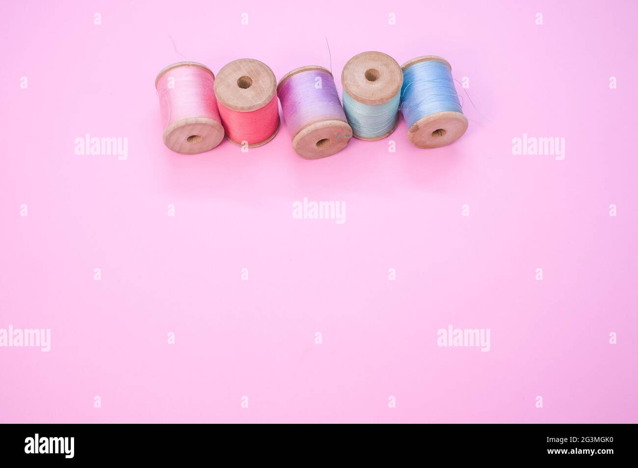 Colorful sewing threads isolated on a pink background with free space ...