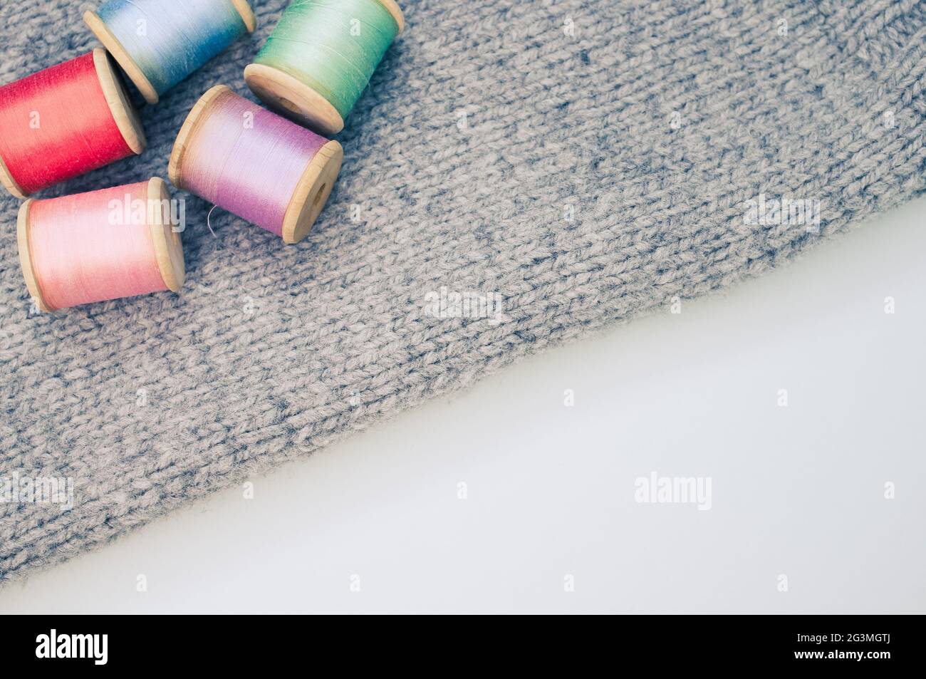 Colorful sewing threads on top of a grey fabric on a white background ...