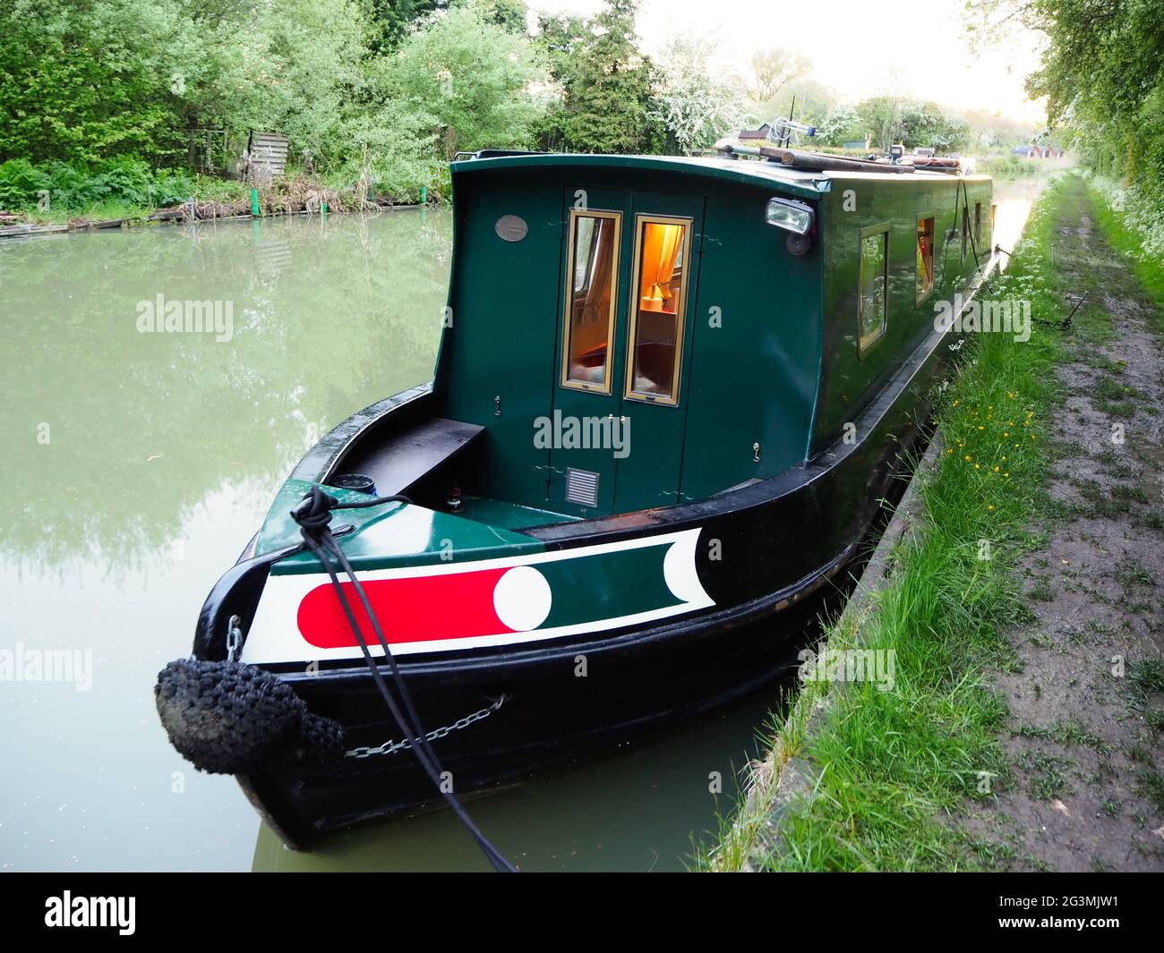 a dark green narrowboat seen moored in the evening Stock Photo