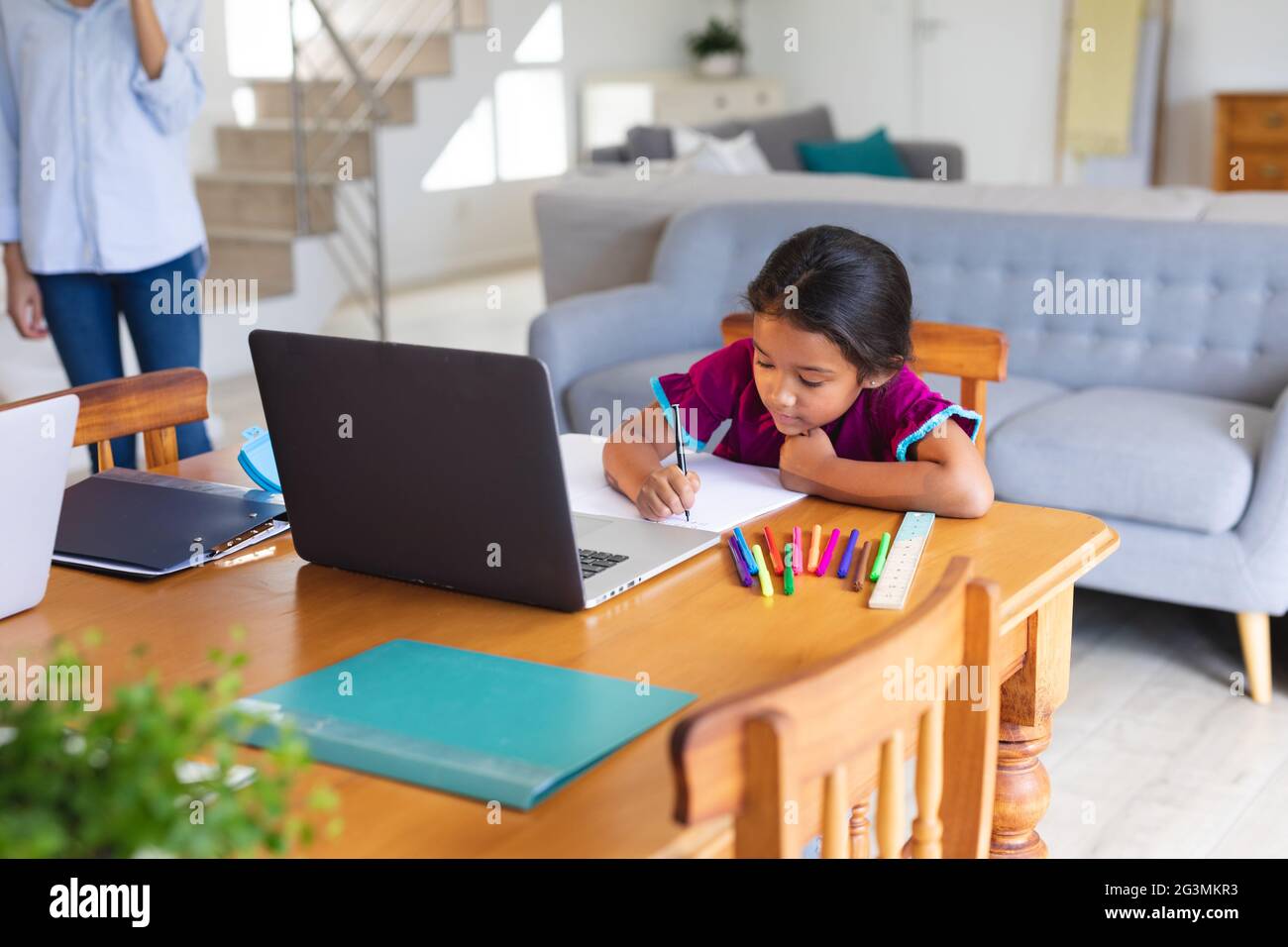 Happy hispanic girl sitting at kitchen table doing school work using laptop Stock Photo