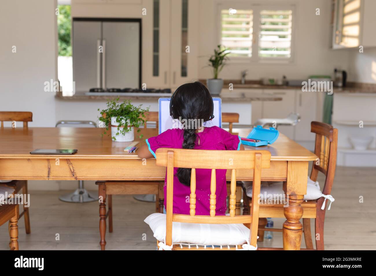Hispanic girl sitting at kitchen table doing school work using laptop Stock Photo