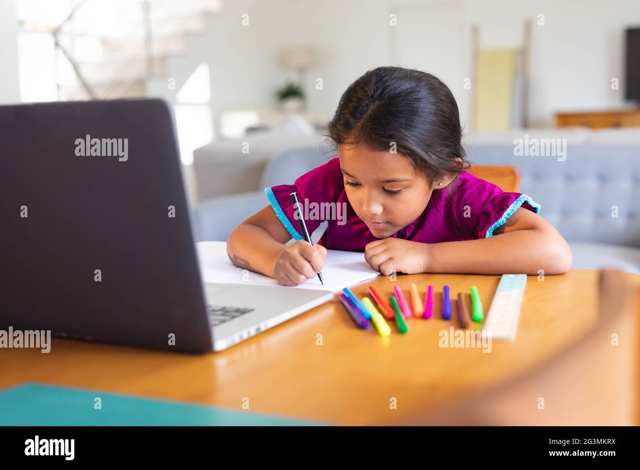 Happy hispanic girl sitting at kitchen table doing school work using laptop Stock Photo