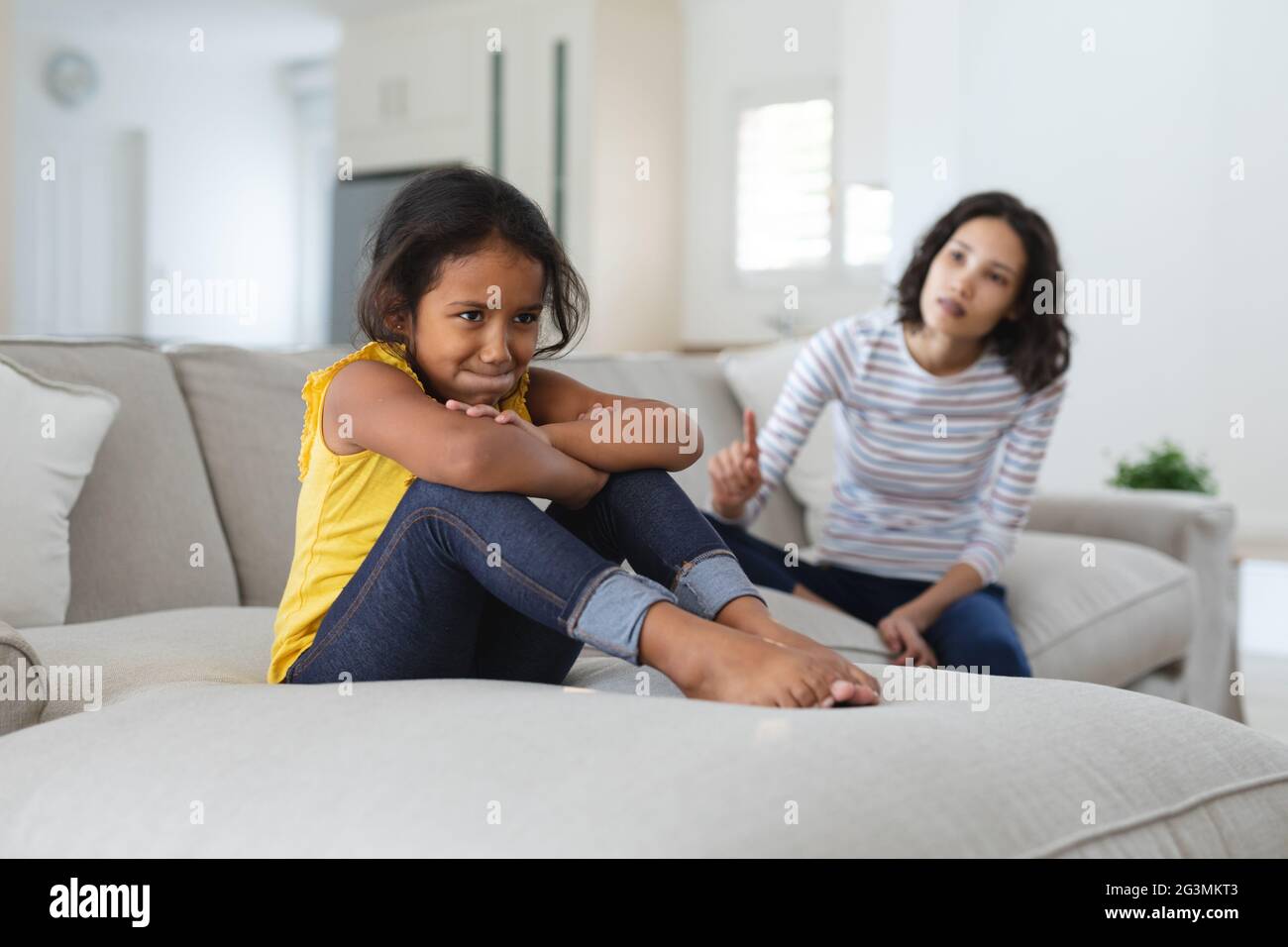 Sad hispanic daughter sitting on couch being told off by mother Stock Photo