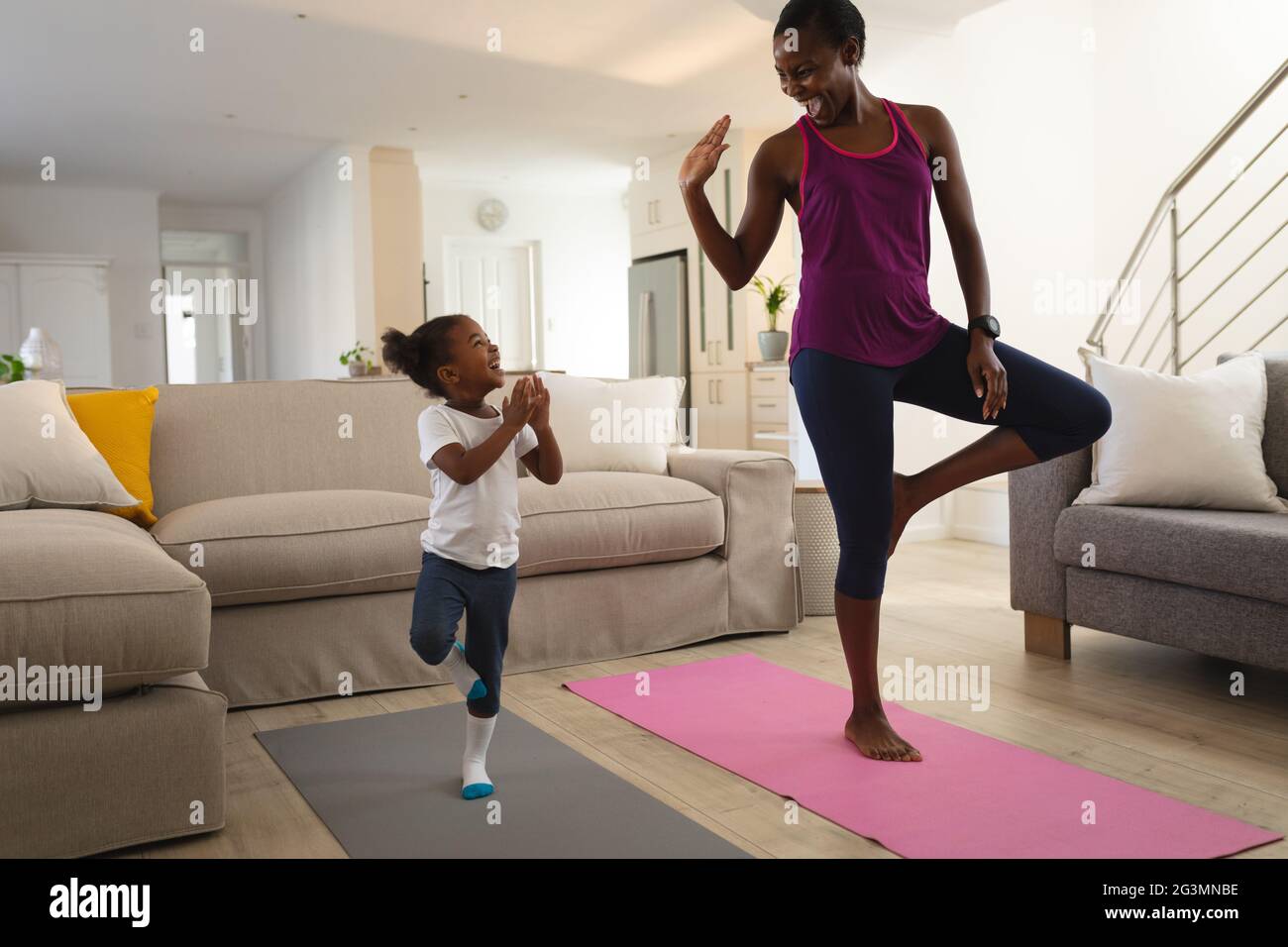 Happy african american mother and daughter practicing yoga, standing on one leg in living room Stock Photo