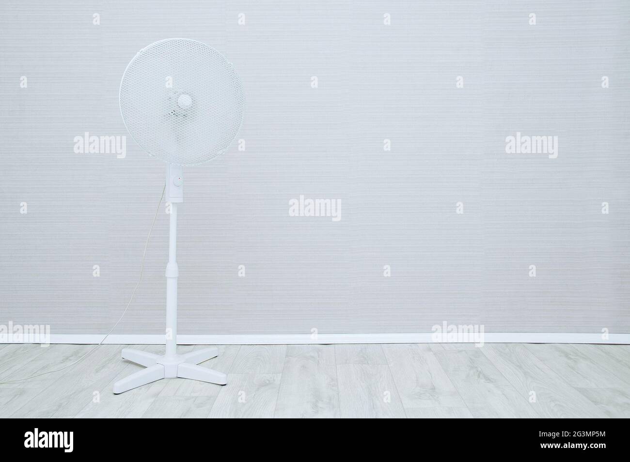 Floor-standing white fan in the interior of the room against the background of a gray wall. Stock Photo