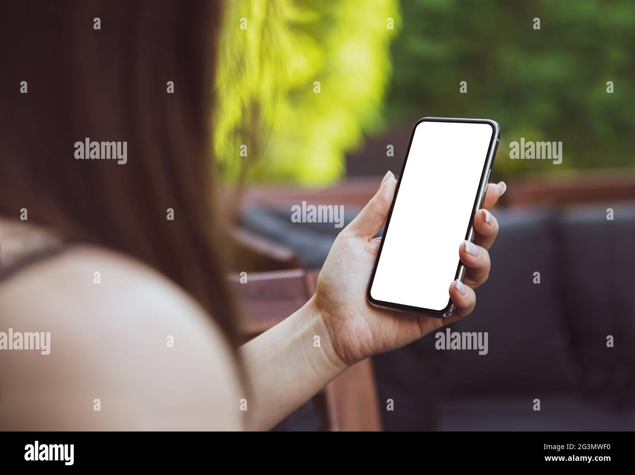 Girl using smartphone blank screen frameless modern design while lying on the sofa in garden Stock Photo