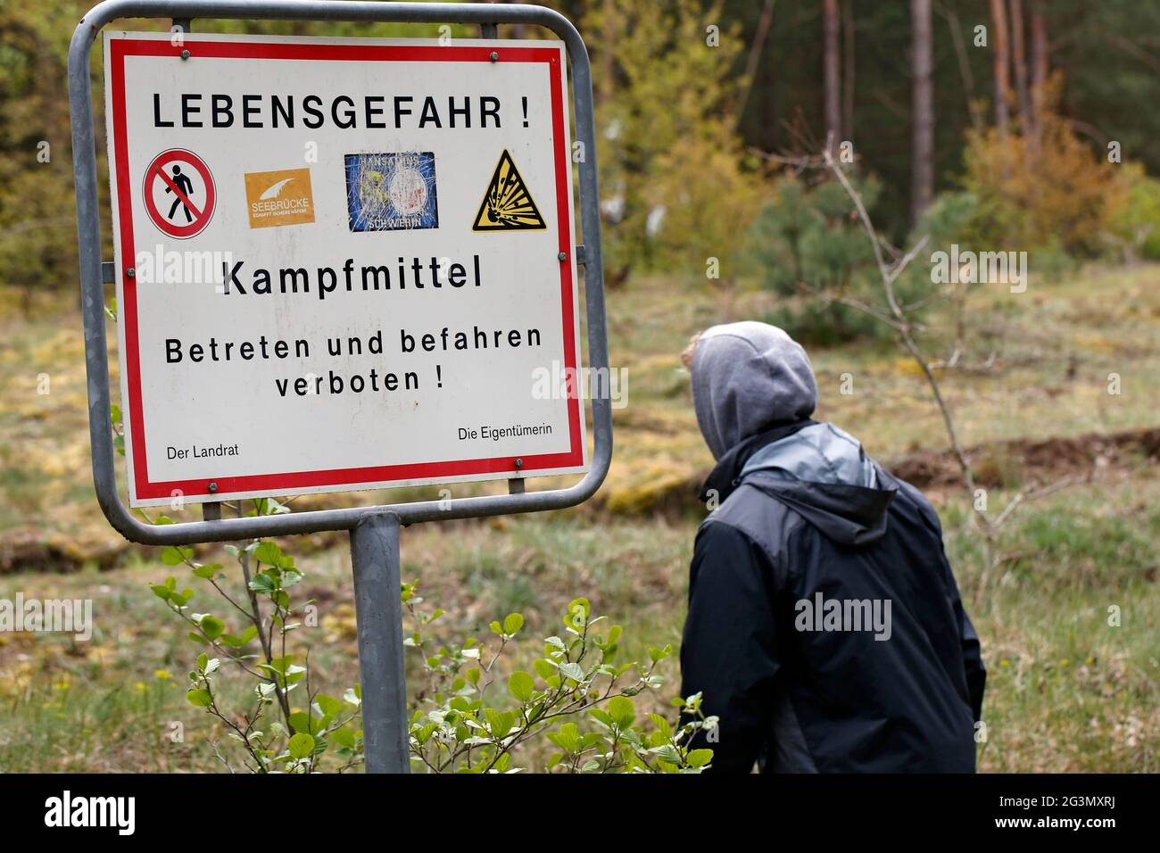 '03.05.2020, Dranse, Brandenburg, Germany - Teenager stands in front of a sign: Danger to life, explosive ordnance, do not enter or drive on. 00S20050 Stock Photo