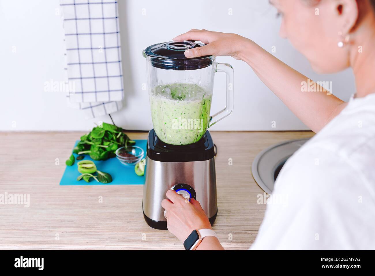 Woman is making homemade healthy smoothie. Vegetarian green cocktail from spinach, broccoli and coconut milk. Morning vitamin charge. Healthy lifestyl Stock Photo
