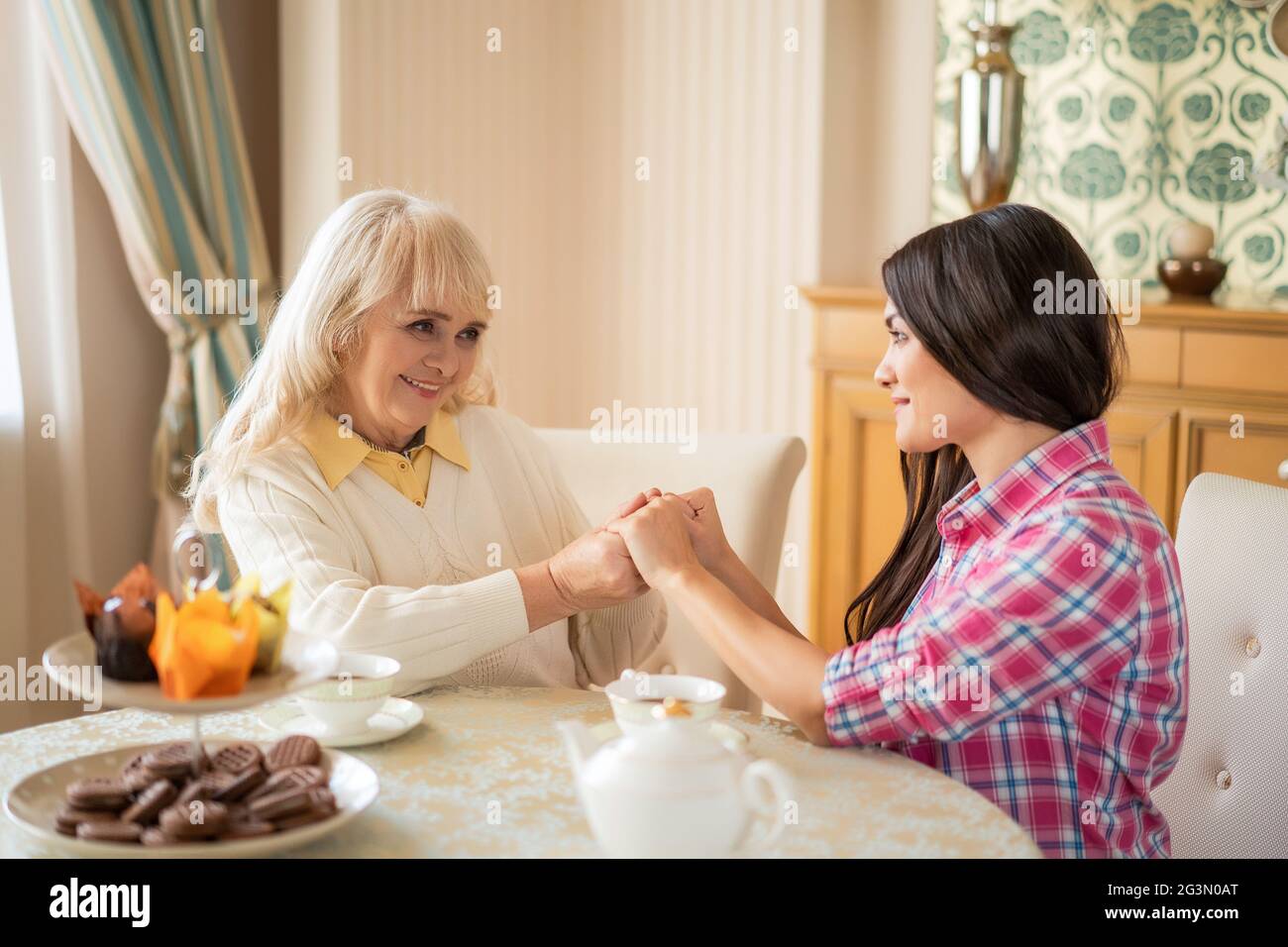 Elderly mother and her daughter holding hands while sitting at the table Stock Photo