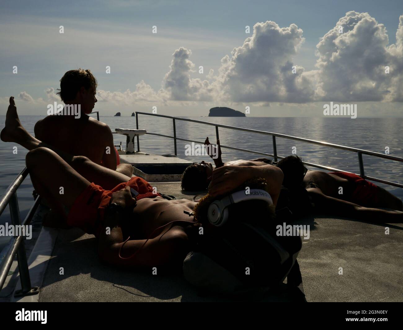 A group of friends lazing in the sun, on a boat from Bali to the Gili islands. Indonesia. Stock Photo