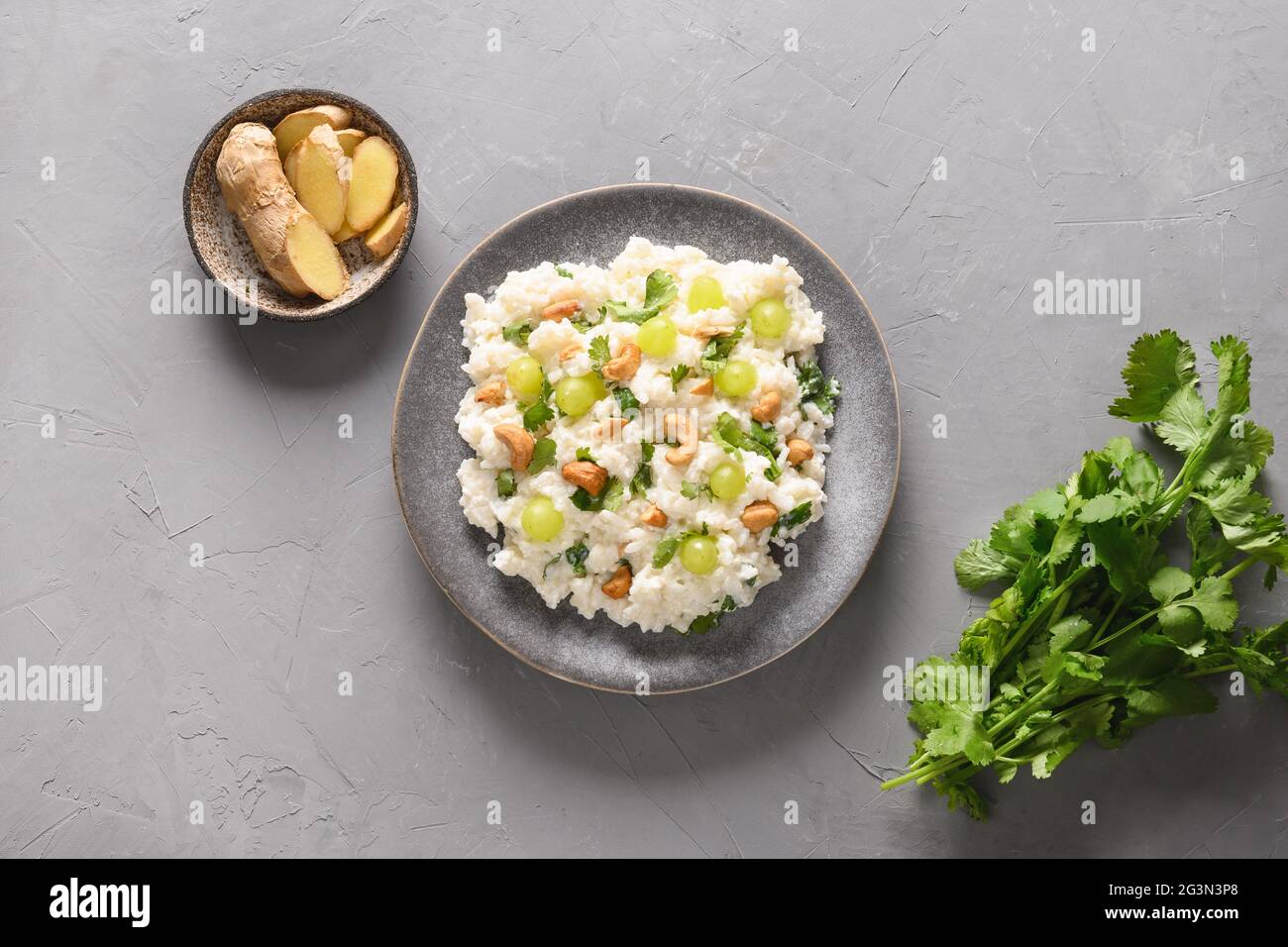 Curd Rice with cashews, grapes, cilantro on a grey background. Indian South cuisine. Top view. Stock Photo