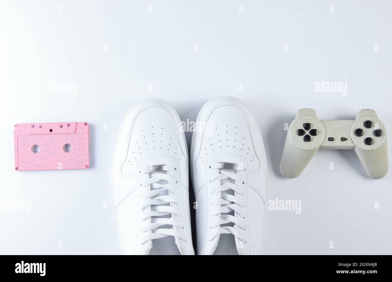 Retro style white sneakers, gamepad , audio cassette on white background. Top view Stock Photo